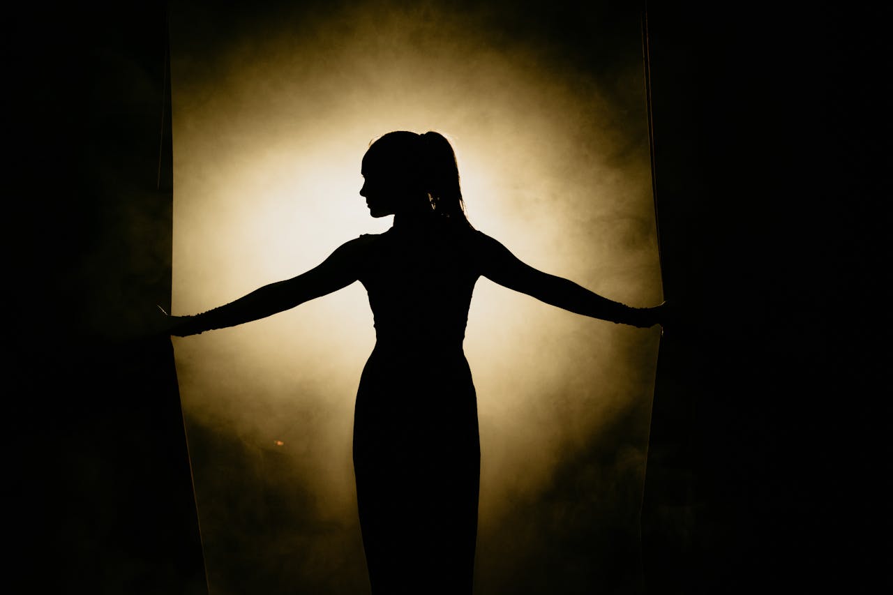 Artistic silhouette of a woman opening stage curtains, surrounded by smoke and spotlight.